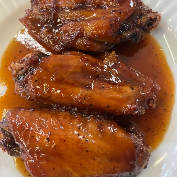 Three glistening Caribbean chicken wings coated in a rich, dark orange sauce on a white plate.